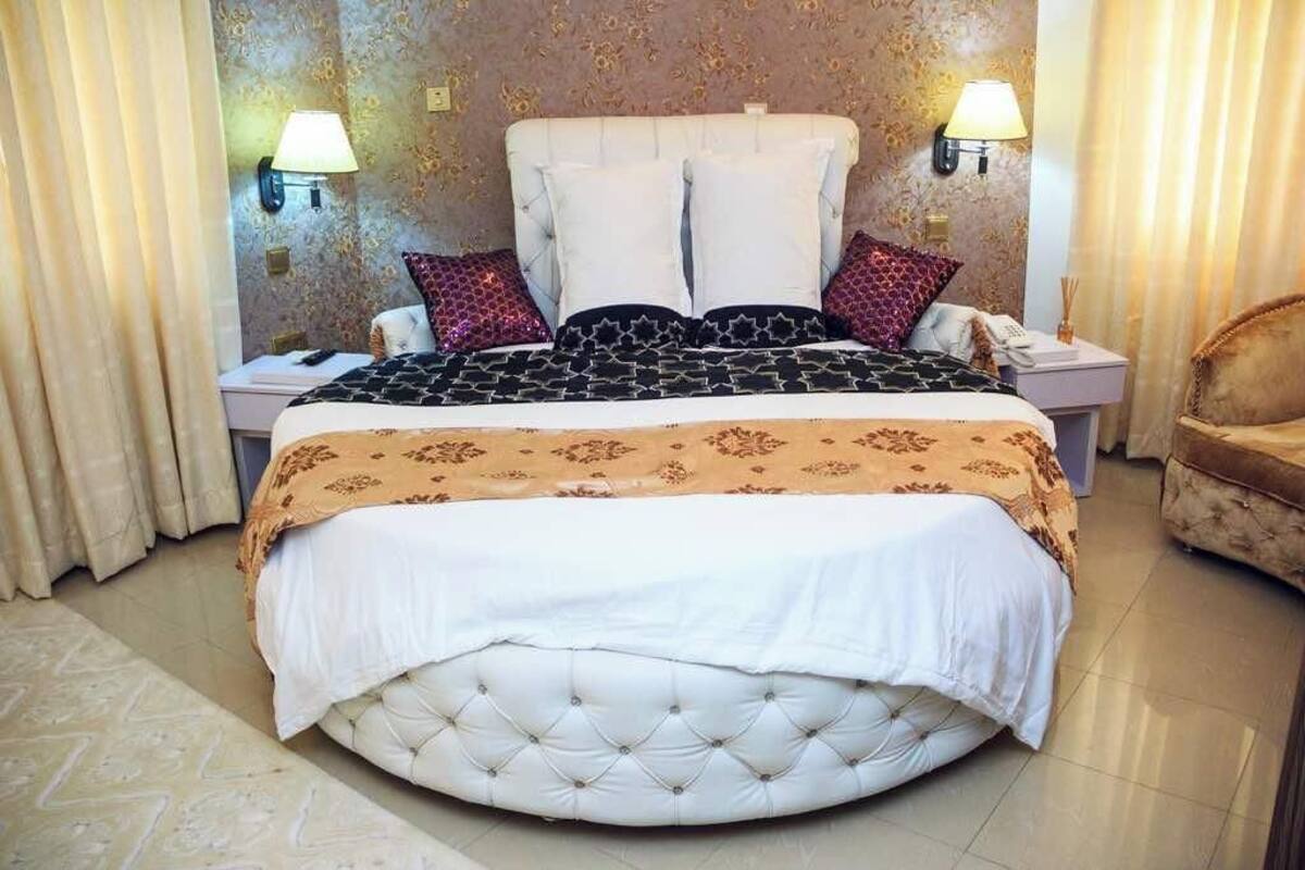 A large, round bed with a tufted headboard, two bedside lamps, and a telephone on the nightstand.