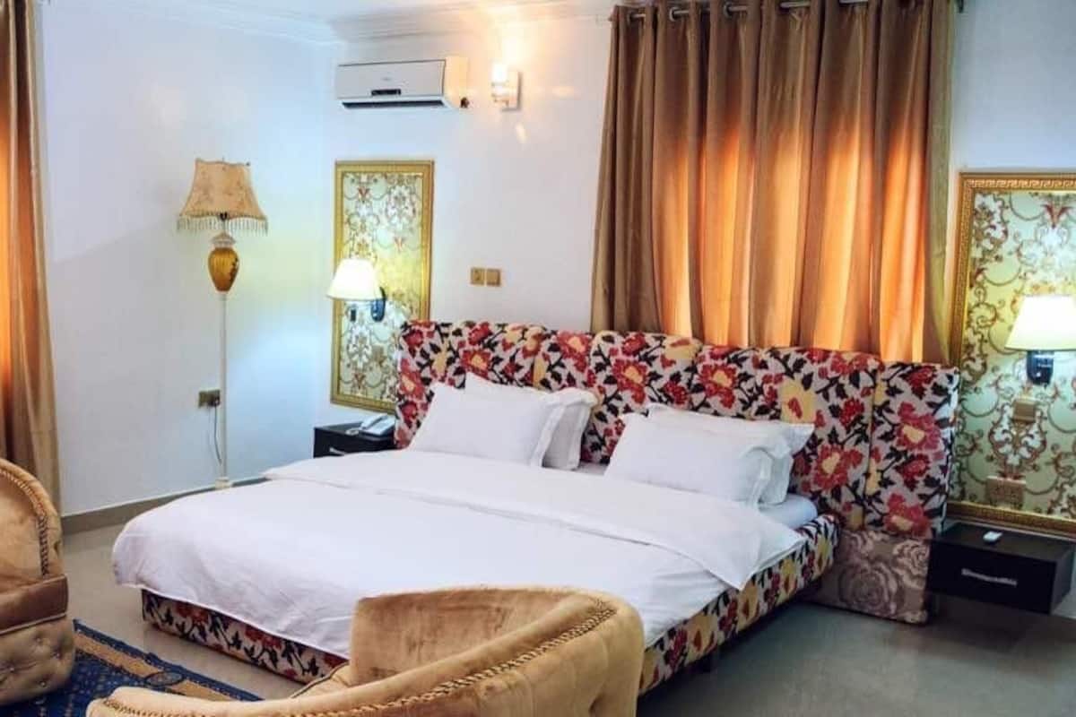 A hotel room with a bed, two chairs, a nightstand, and a lamp.