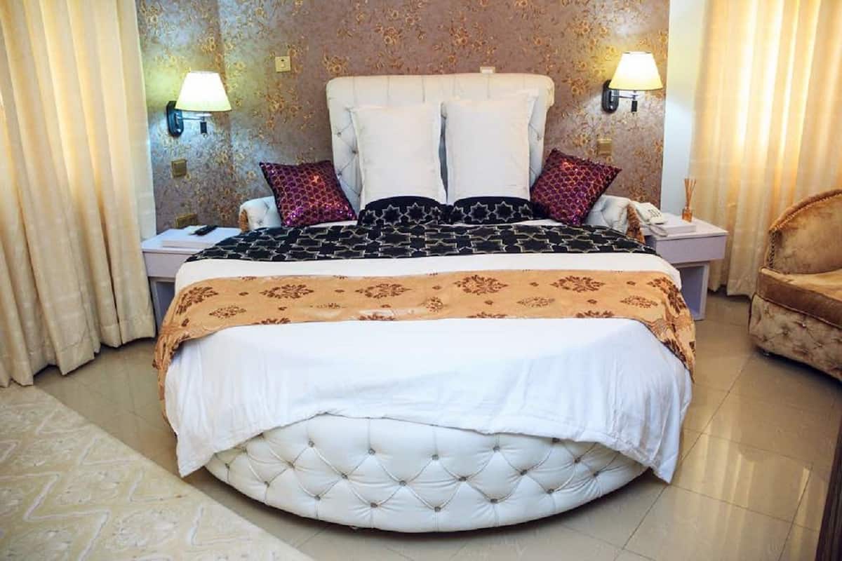 A large, round bed with a tufted headboard, two bedside tables, and a nightstand with a lamp.