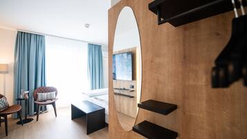 Una habitación de hotel moderna con una pared de acento de madera, un espejo grande, un televisor de pantalla plana, una cama, un escritorio y una silla.