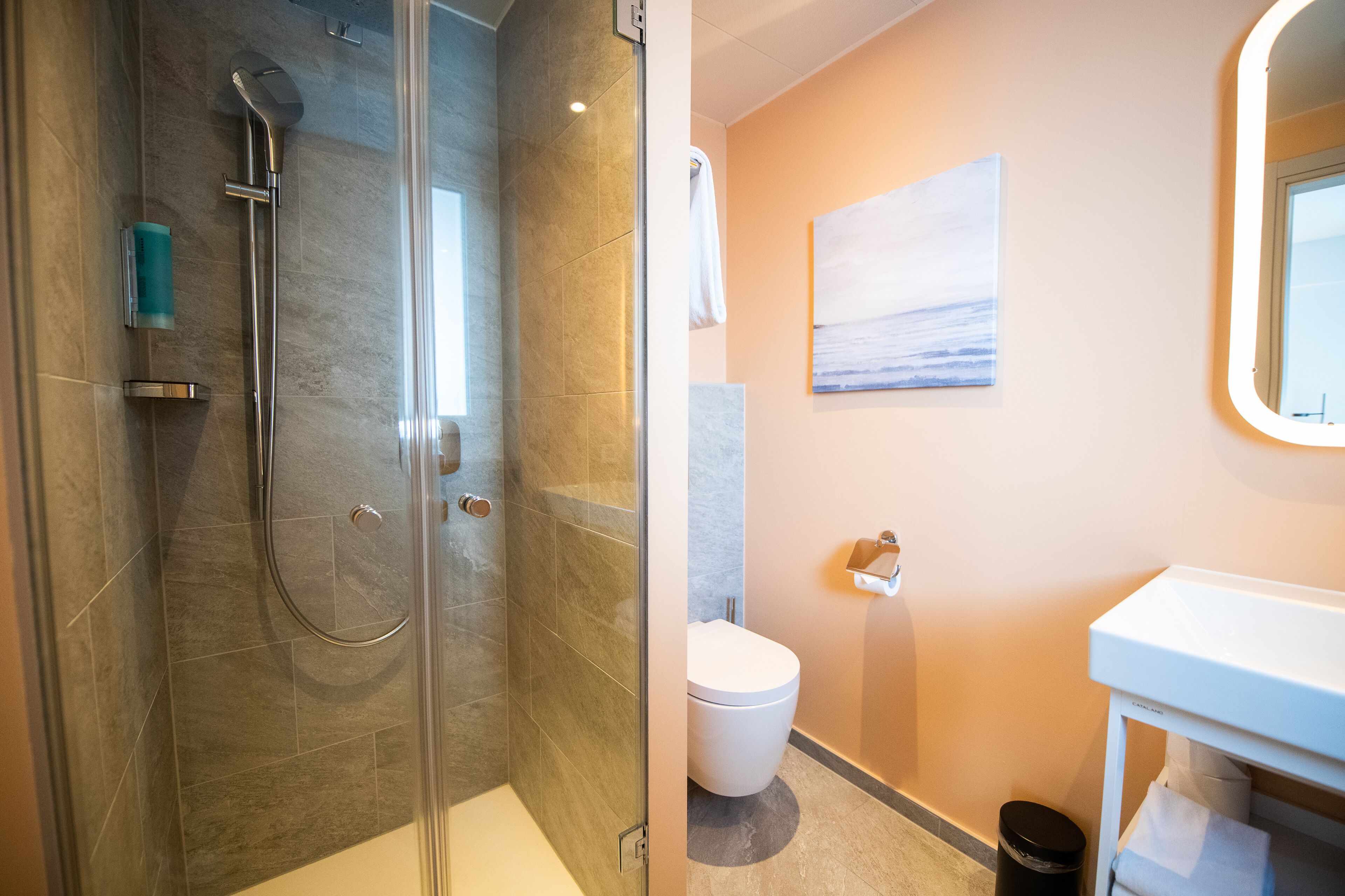 A modern bathroom with a glass-enclosed shower, a white toilet, and a sink with a mirror.