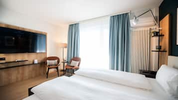 Une chambre d’hôtel avec un grand lit, un bureau, une chaise, une télévision et une fenêtre avec des rideaux.