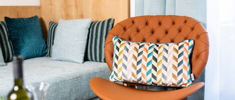 Un salon moderne avec un fauteuil en cuir capitonné, un coussin à motifs, un canapé gris et une tête de lit en bois.