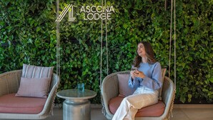 Una mujer sentada en una silla de mimbre en una habitación con un muro cubierto de plantas y una mesita.