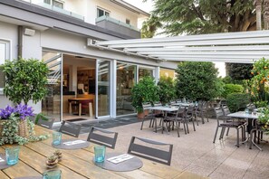 Un espace extérieur aménagé avec des tables et des chaises, un coin salon abrité et des plantes en pot.