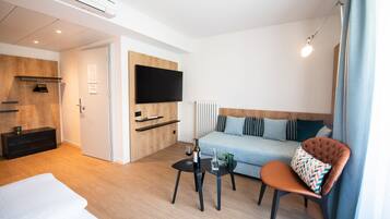 A modern hotel room with a sofa, a chair, a small table, a TV, and a bed.