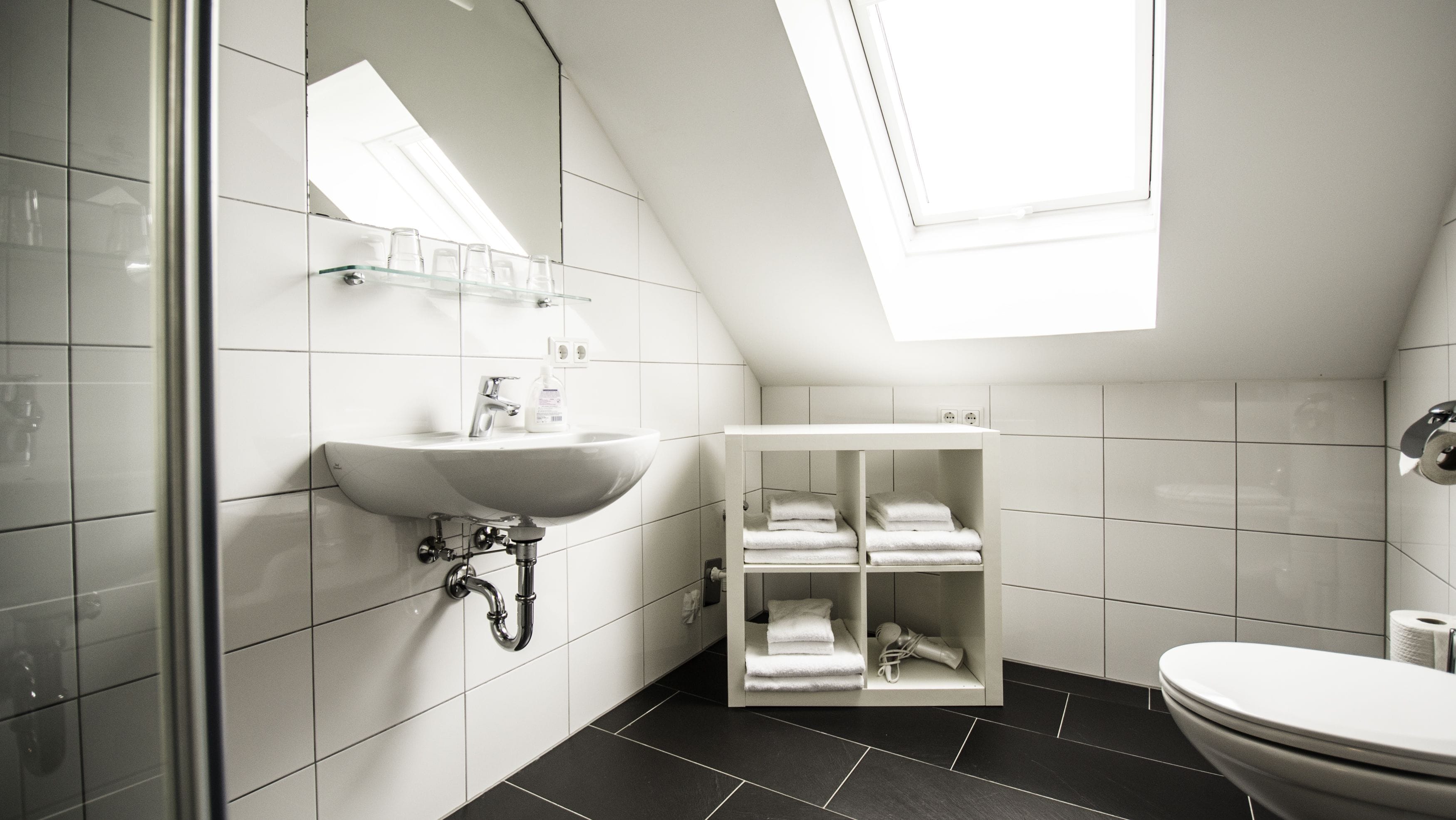 Un bagno moderno con un lucernario, un lavandino bianco e un water.
