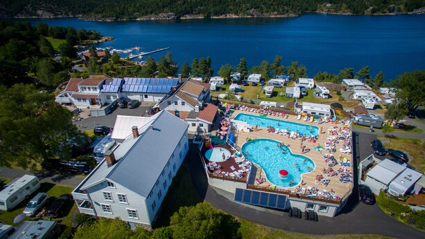 A large swimming pool surrounded by RVs and mobile homes, with a lake in the background. - Sørlandet Feriesenter (Risør)