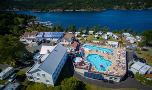 A large swimming pool surrounded by RVs and mobile homes, with a lake in the background. - Sørlandet Feriesenter (Risør)