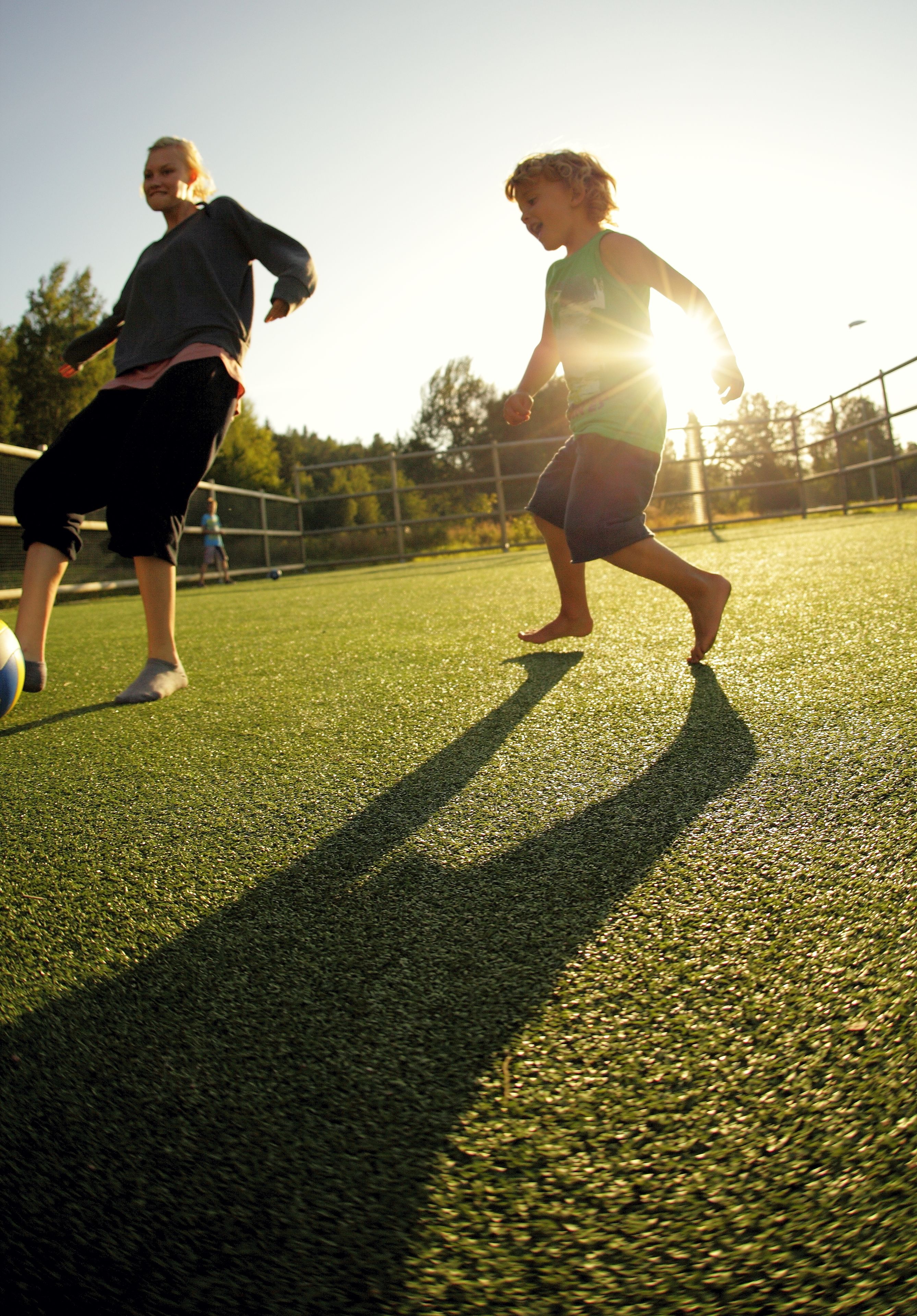 A person playing soccer on a green field with shadows cast by the sun.