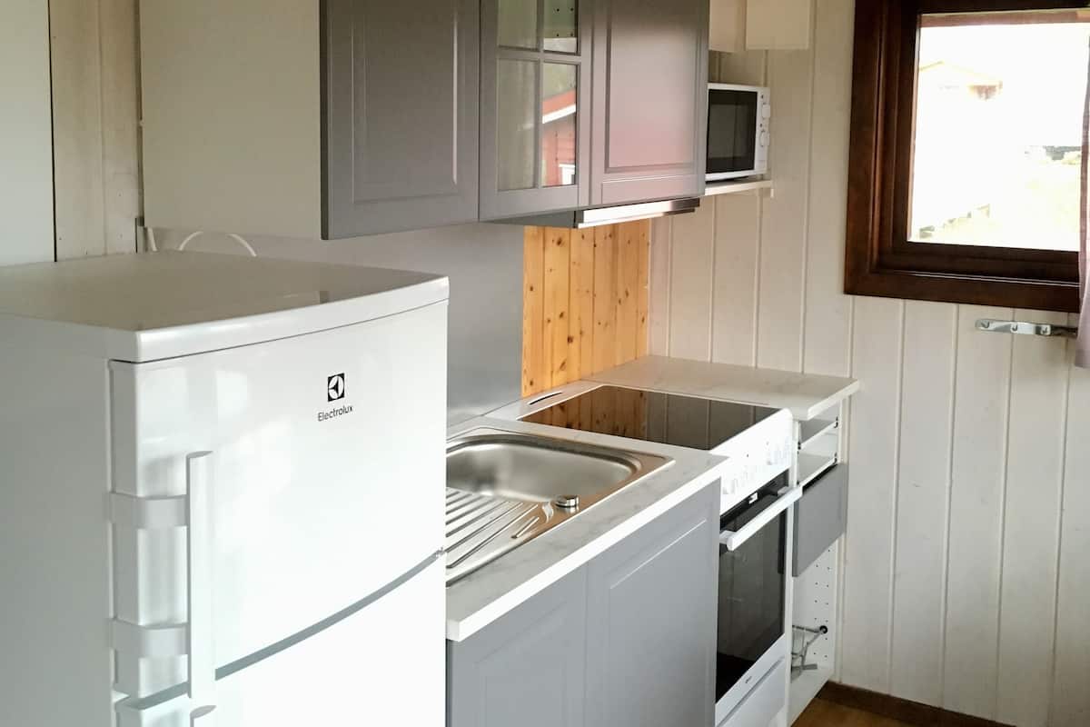 A compact kitchen with white cabinets, a built-in microwave, a refrigerator, and a window with a view.
