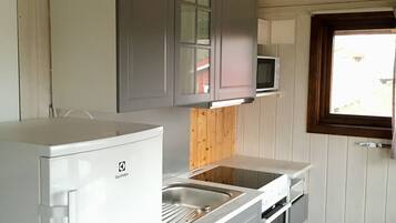 Cozinha compacta com armários brancos, micro-ondas embutido, geladeira e janela com vista.