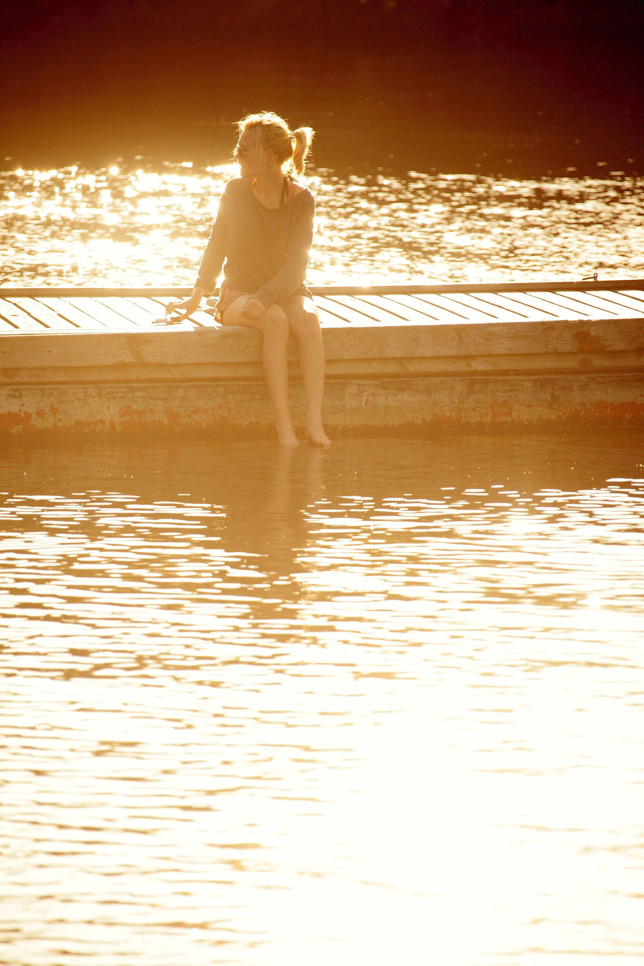 Iemand zit aan het water tijdens de zonsondergang.