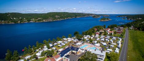 An aerial view of a lakeside campground with RVs, a swimming pool, and a road.