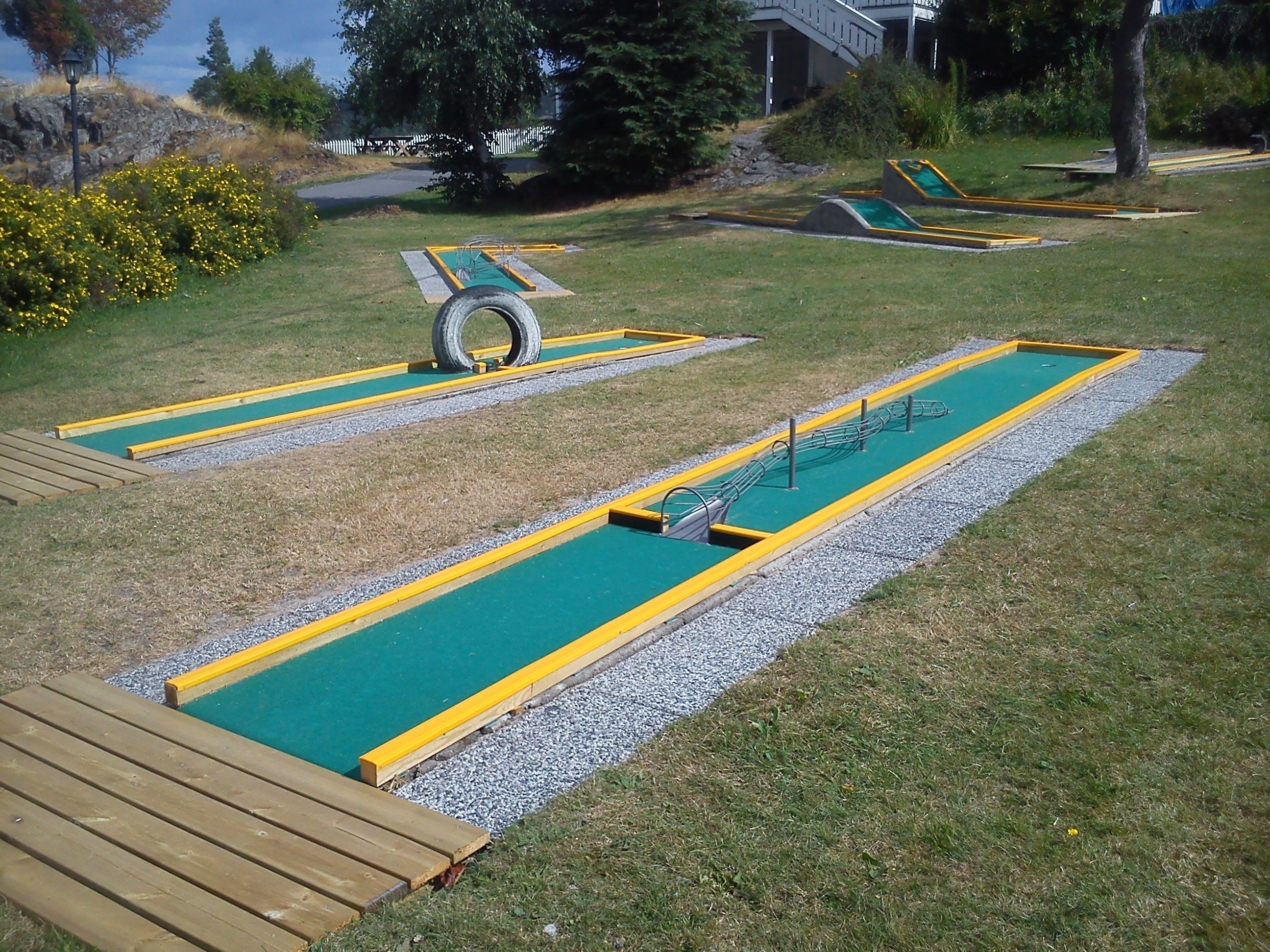 Ein Minigolfplatz mit zwei Putting-Greens, einer Holzterrasse und einer Reifen-Hindernisbahn.