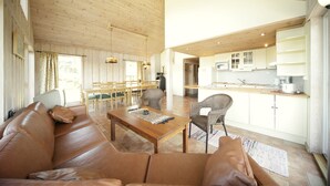 A spacious living area with a wooden ceiling, a leather sofa, a wooden coffee table, and a dining area with chairs and a table. - Sørlandet Feriesenter (Risør)