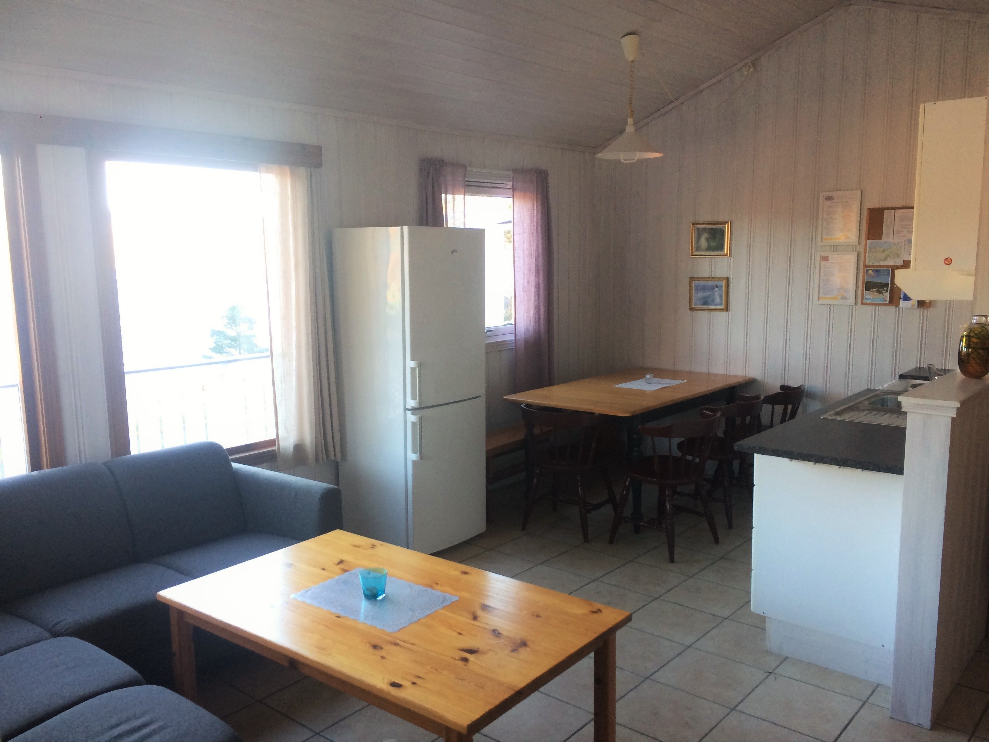 Un espacio habitable compacto con un sofá, una mesita con una taza, un refrigerador, una mesa de comedor con sillas, y una zona de cocina con un fregadero y encimera.
