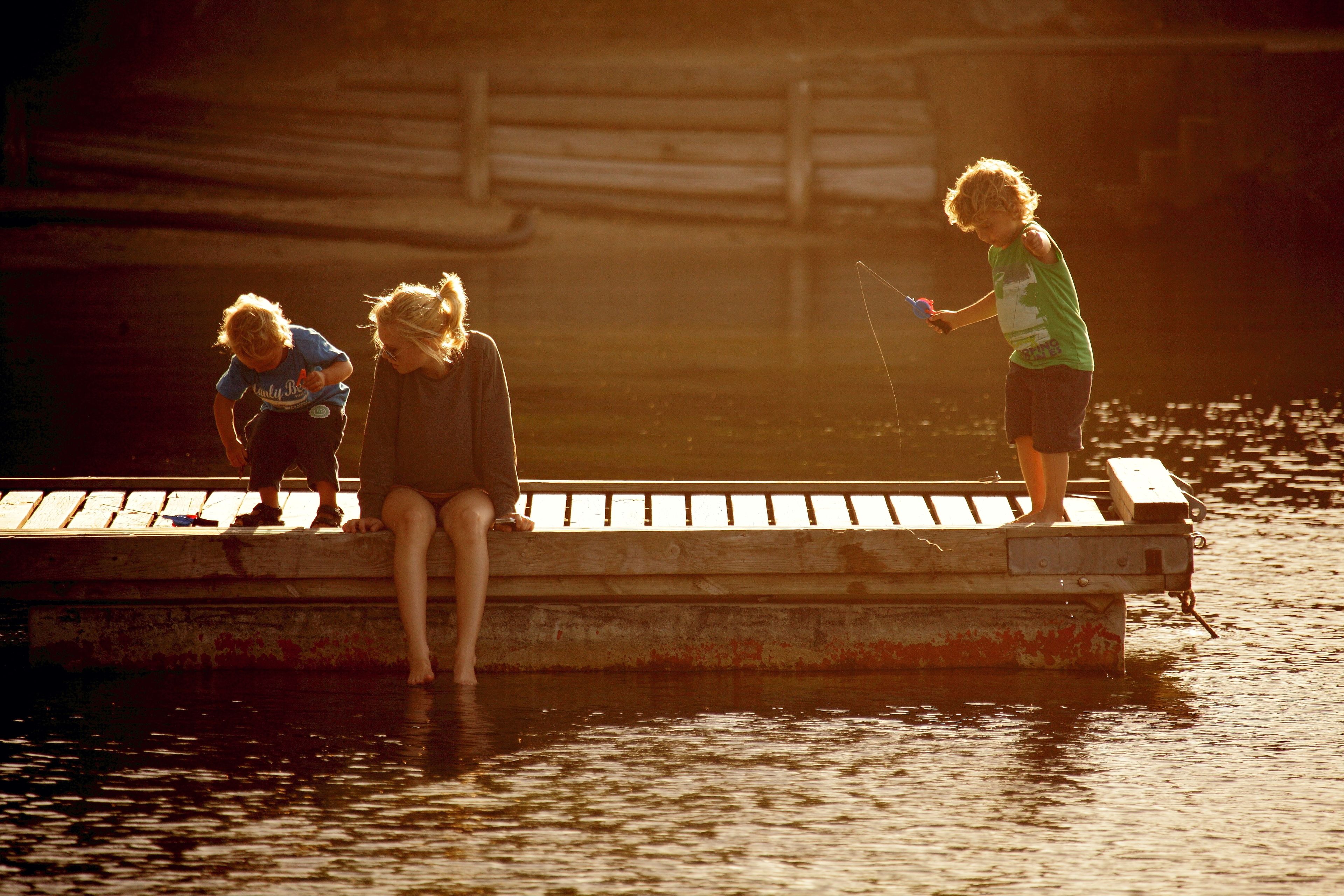 Three children on a wooden dock by a body of water.
