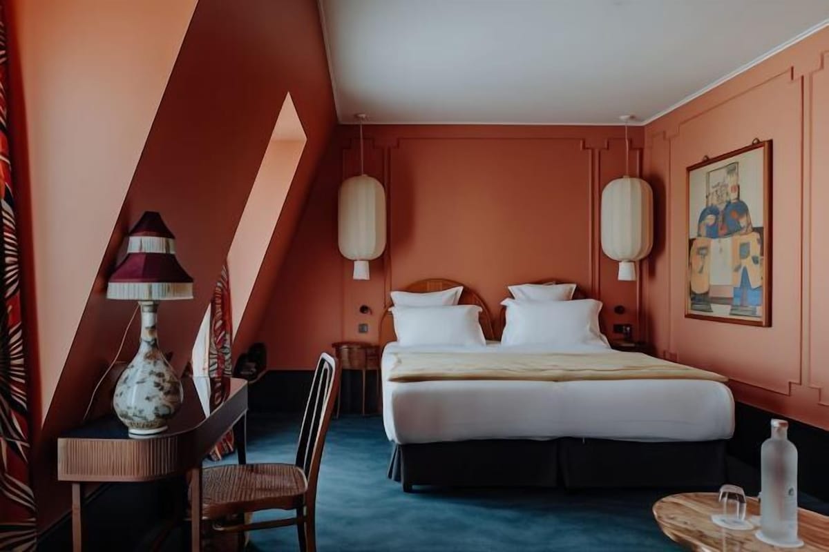 A hotel room with a bed, bedside tables, a chair, a lamp, and a painting on the wall.
