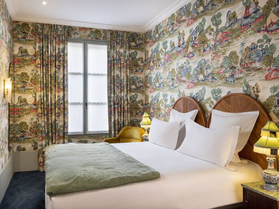 A hotel room with a large bed, two bedside tables with lamps, a window with curtains, and a wall with a mural.
