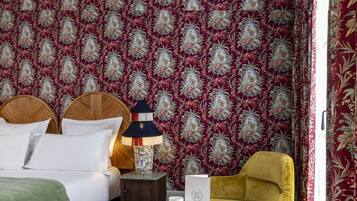 A hotel room with a large bed, a nightstand with a lamp, a chair, and a wall with a floral pattern.