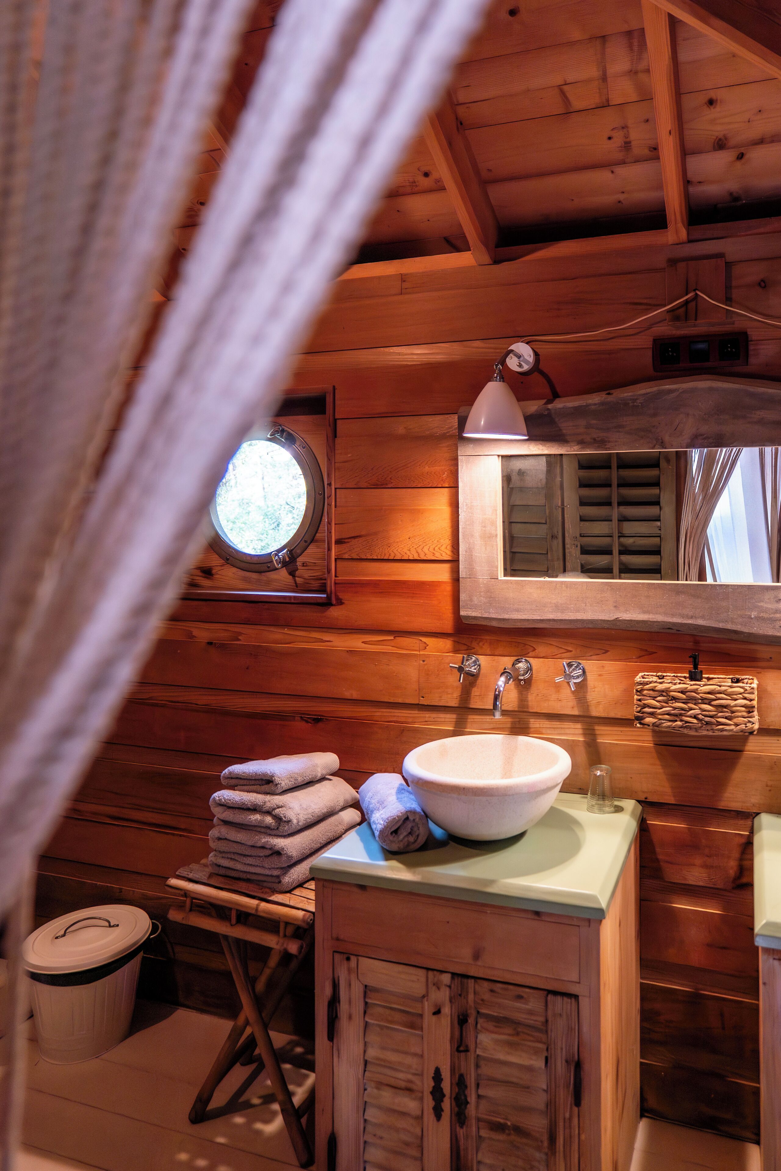 A wooden cabin bathroom with a round window, a sink, and a mirror.