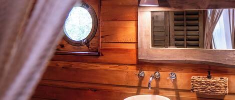 A wooden cabin bathroom with a round window, a sink, and a mirror.