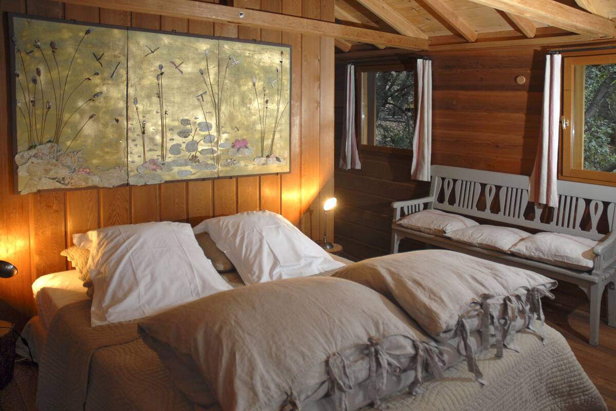 A wooden cabin bedroom with two beds, a bench, and a large painting on the wall.