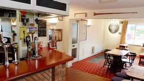 A bar area with a brick counter, multiple taps, and a dartboard on the wall. There are tables and chairs in the dining area, and a red carpet on the floor. - The Trout Cafe (Llanwrtyd Wells)