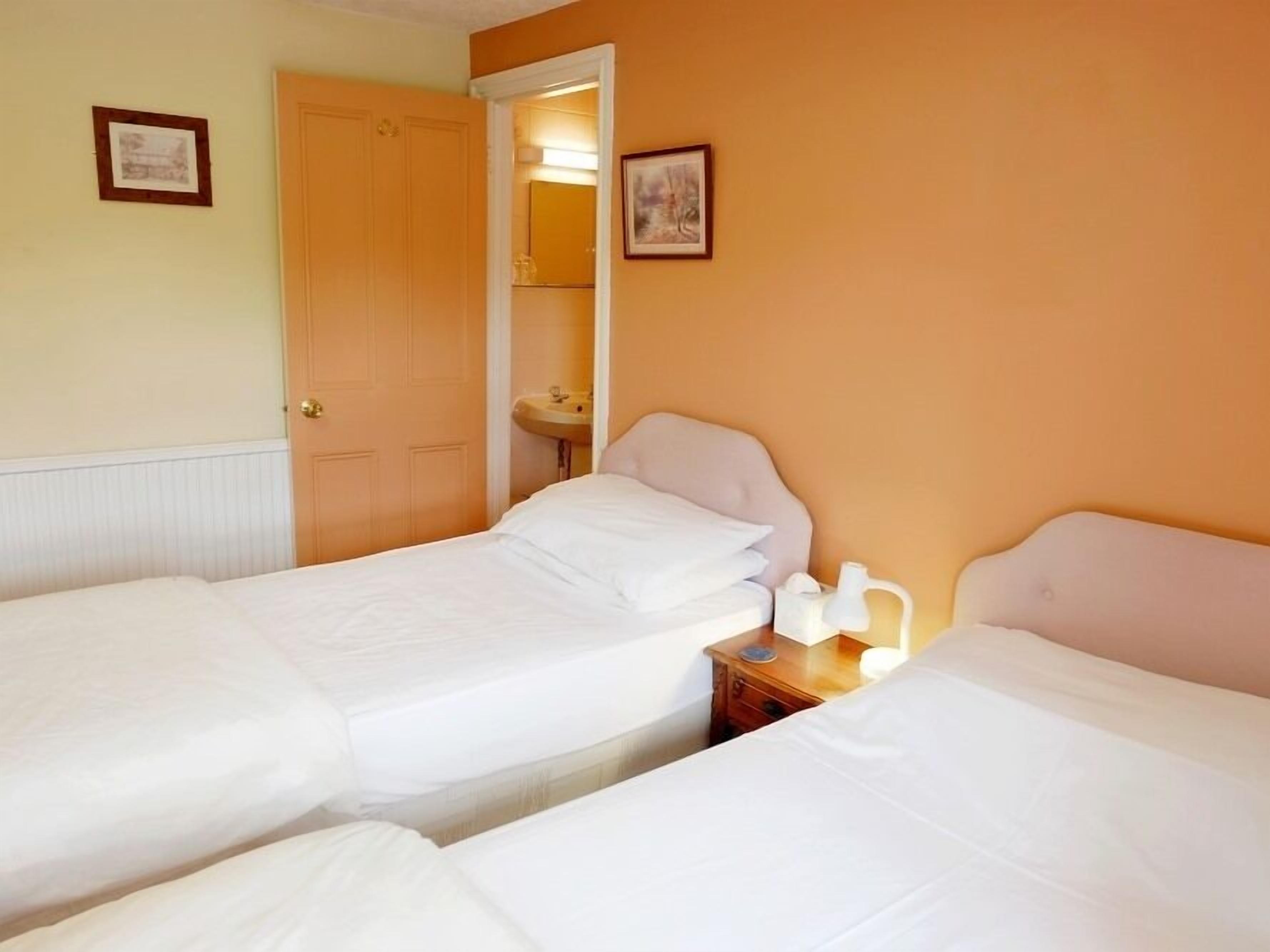 A hotel room with two single beds, a bedside table with a lamp, a mirror, and a small bathroom with a sink.