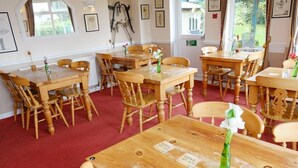 A dining area with multiple wooden tables and chairs, some with name tags, and a red carpeted floor. - The Trout Cafe (Llanwrtyd Wells)