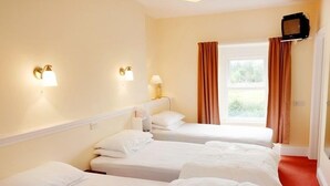 A hotel room with three single beds, a television mounted on the wall, and a window with curtains. - The Trout Cafe (Llanwrtyd Wells)