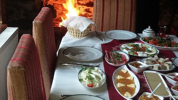 Un restaurante con horno de piedra, una mesa dispuesta con diversos platos y sillas con cojines a rayas.