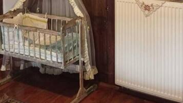 A room with a rustic stone ceiling, a wooden floor, a traditional crib with a canopy, a radiator, and a mirror with a decorative frame.