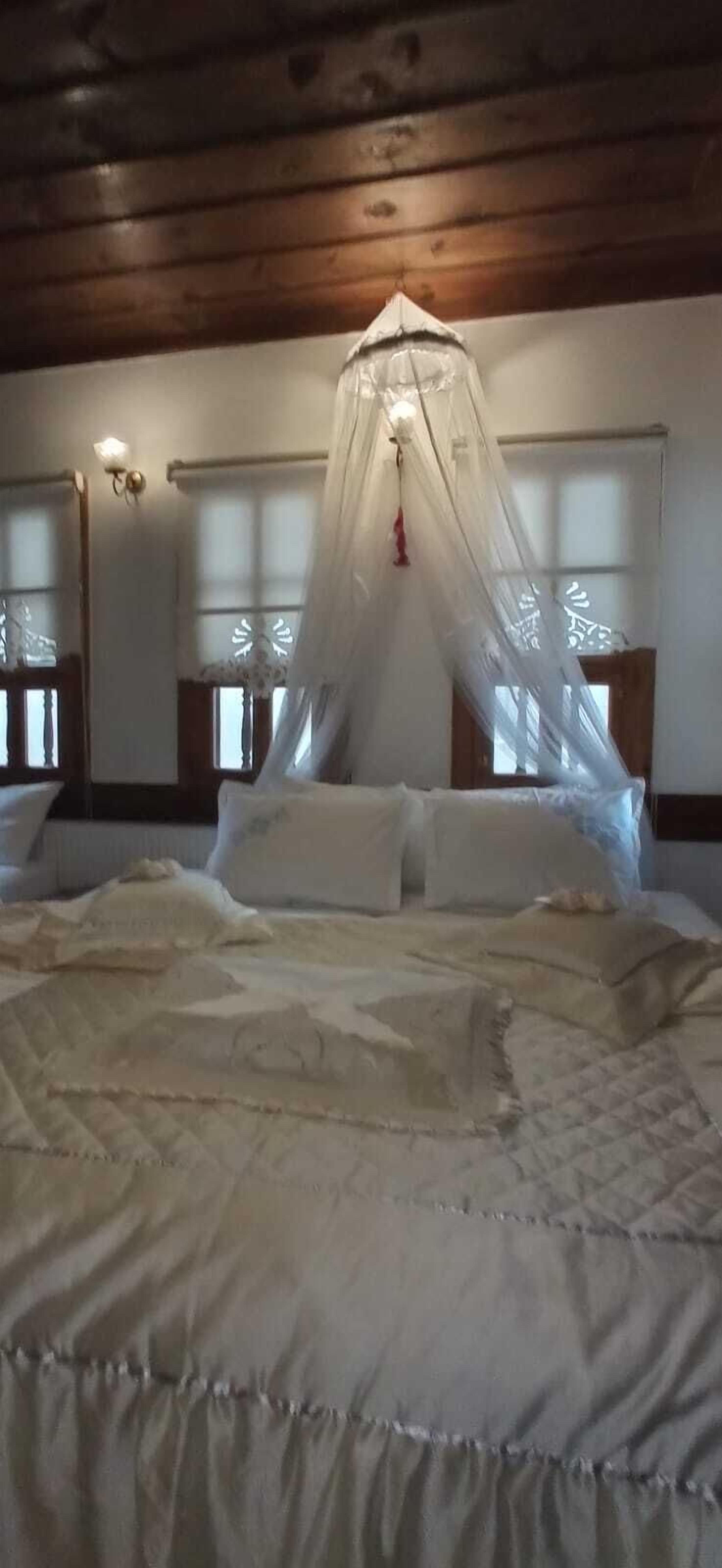 A bed with a canopy, wooden ceiling beams, and two bedside tables with lamps.