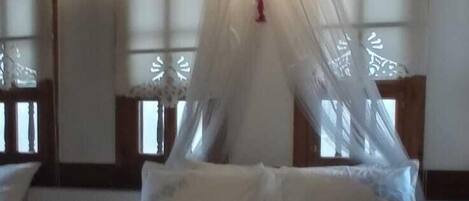 A bed with a canopy, wooden ceiling beams, and two bedside tables with lamps.
