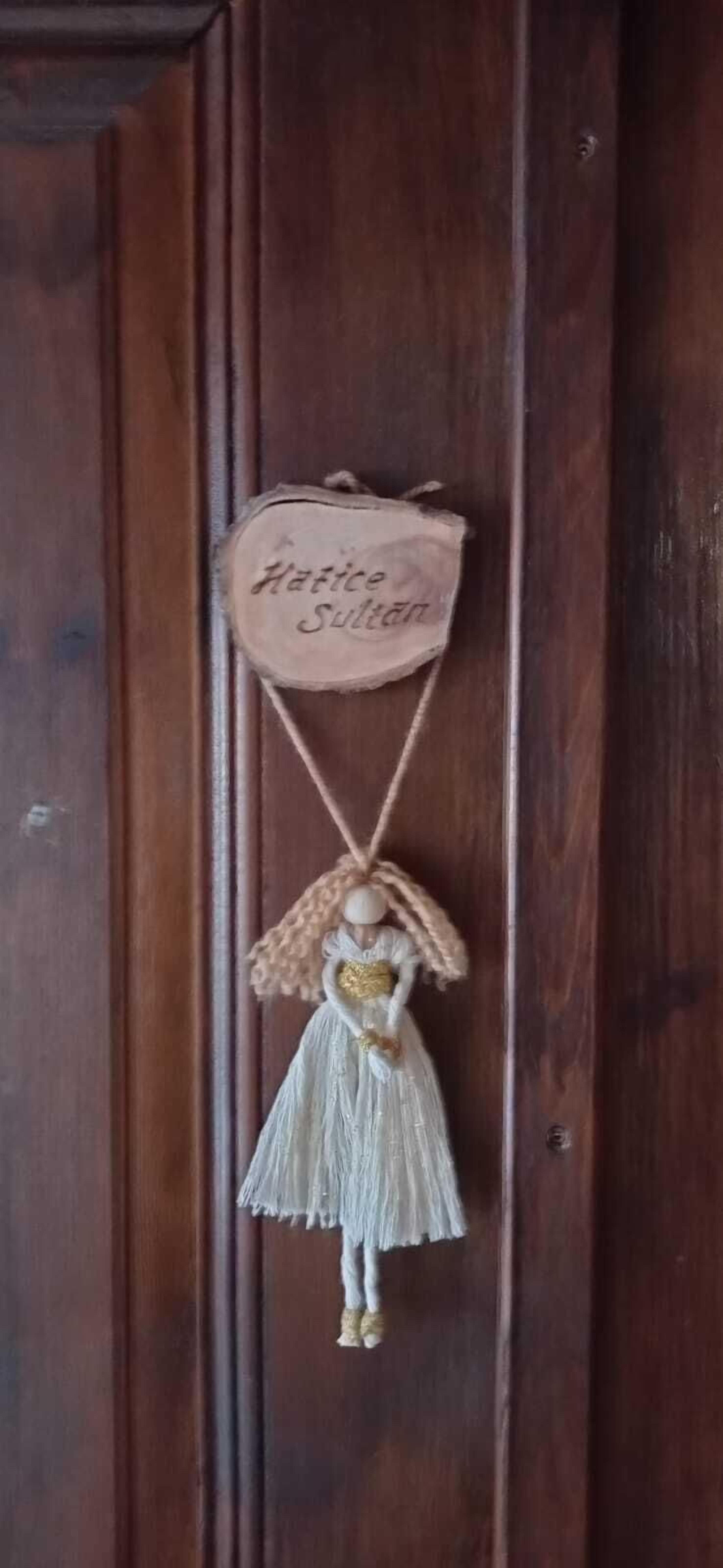 A wooden door with a hanging ornament featuring a figure in a dress and a sign that reads "Hattice Sulten".