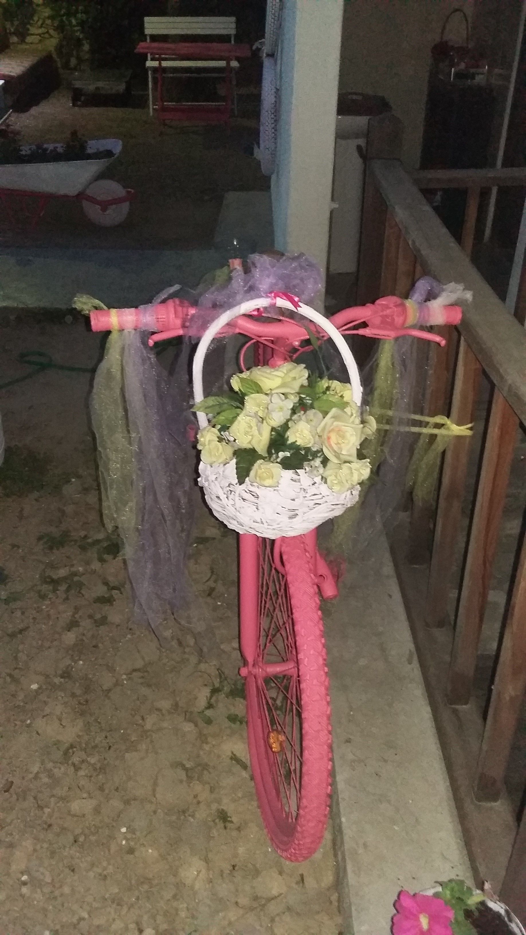 Una bicicleta rosa con una cesta llena de flores amarillas, estacionada sobre una superficie de concreto.
