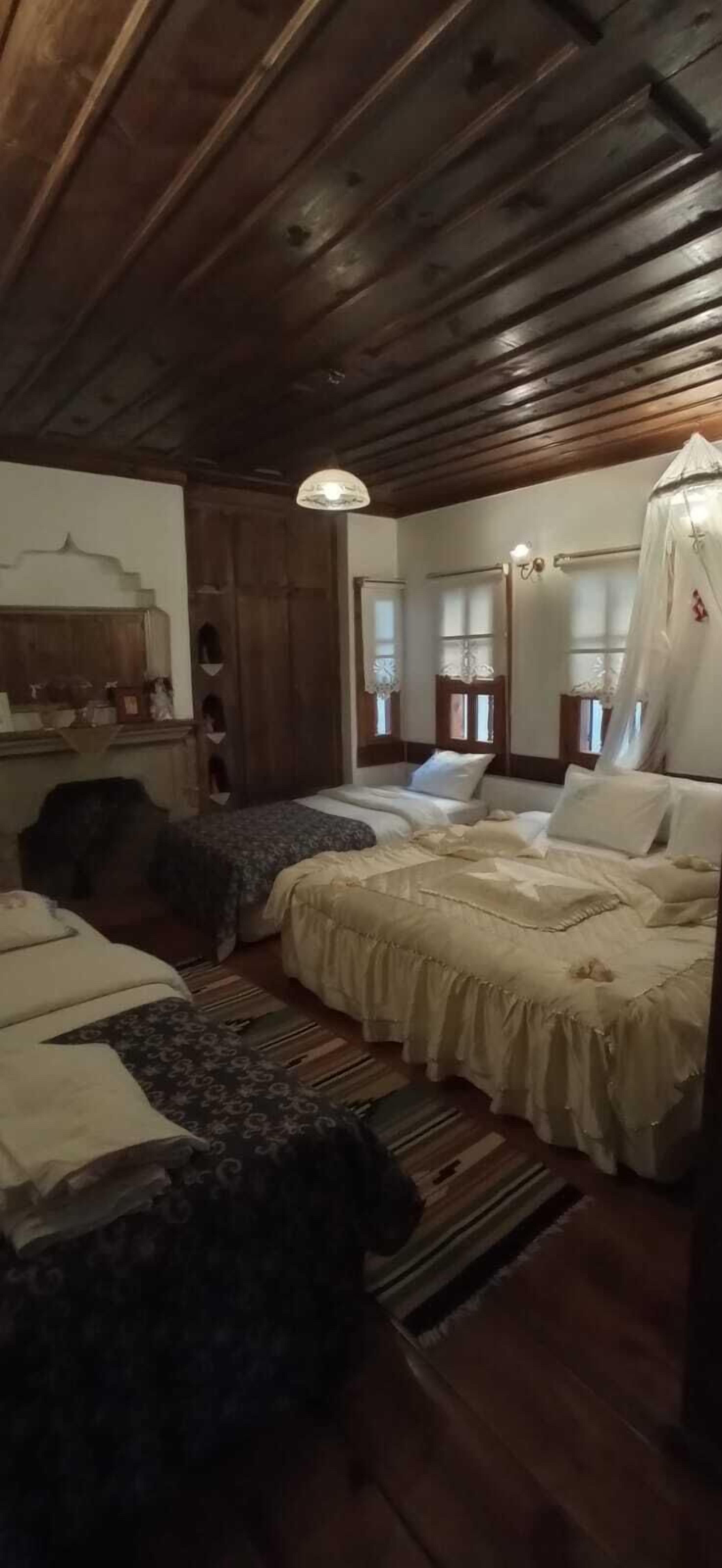 Una habitación rústica con techos y paredes de madera, dos camas con sábanas blancas, un aparador de madera y un espejo con marco decorativo.