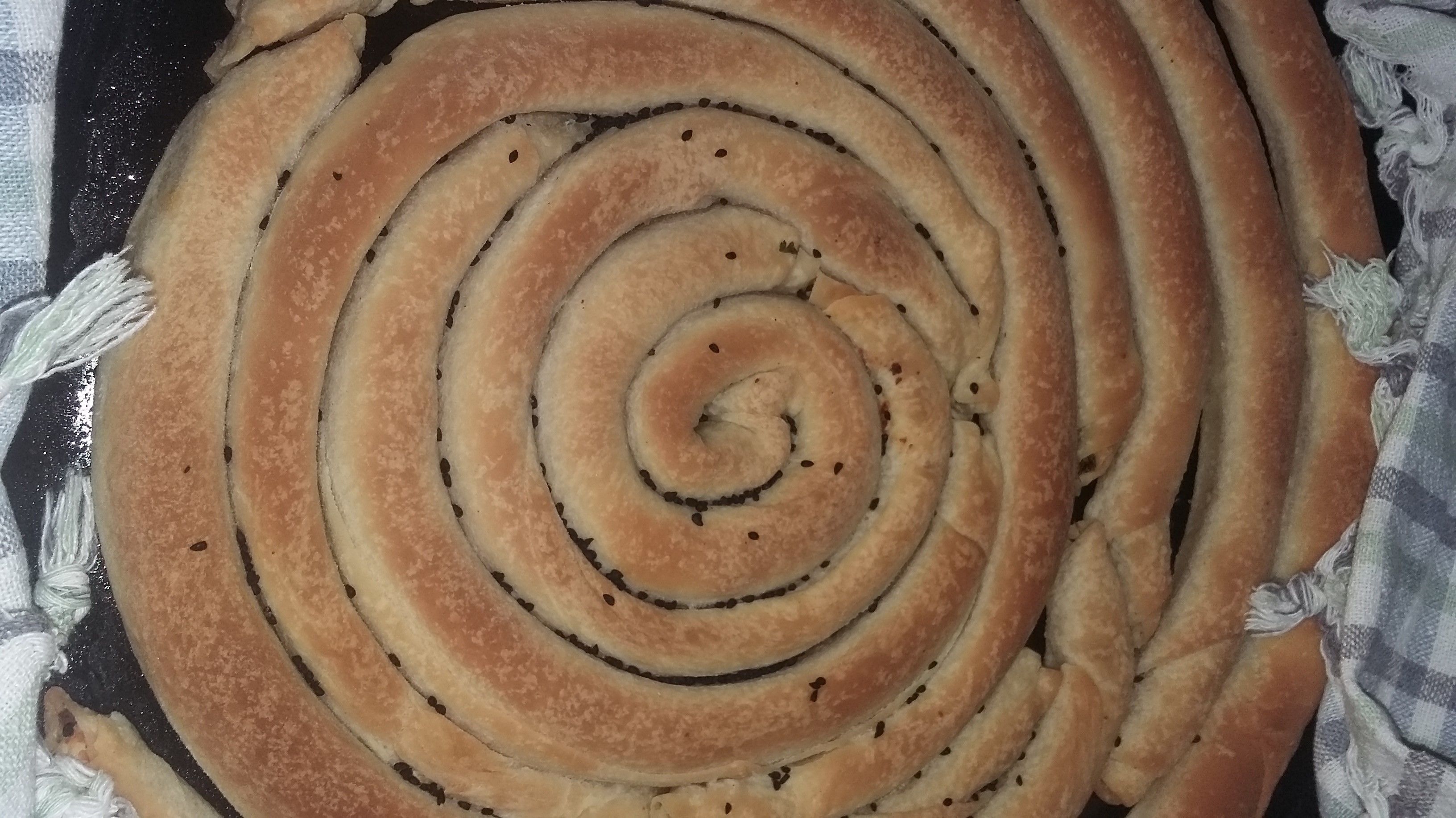 Une pâtisserie en forme de spirale, dotée d’une croûte dorée, posée sur un tissu à carreaux.