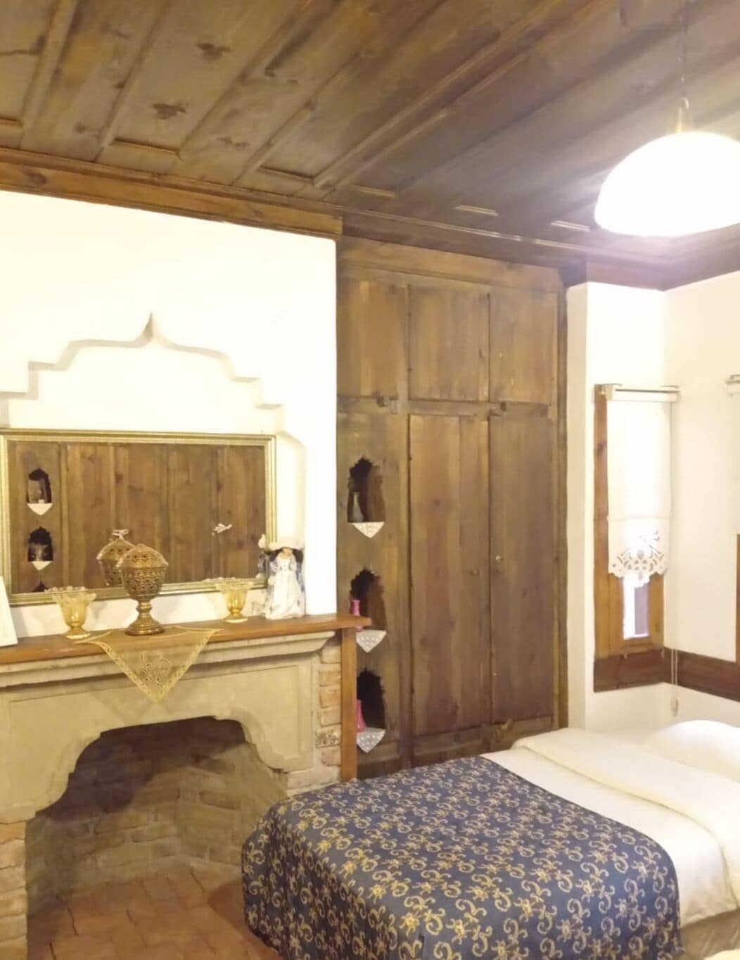 Una habitación con chimenea, un armario de madera y una cama con colcha estampada.