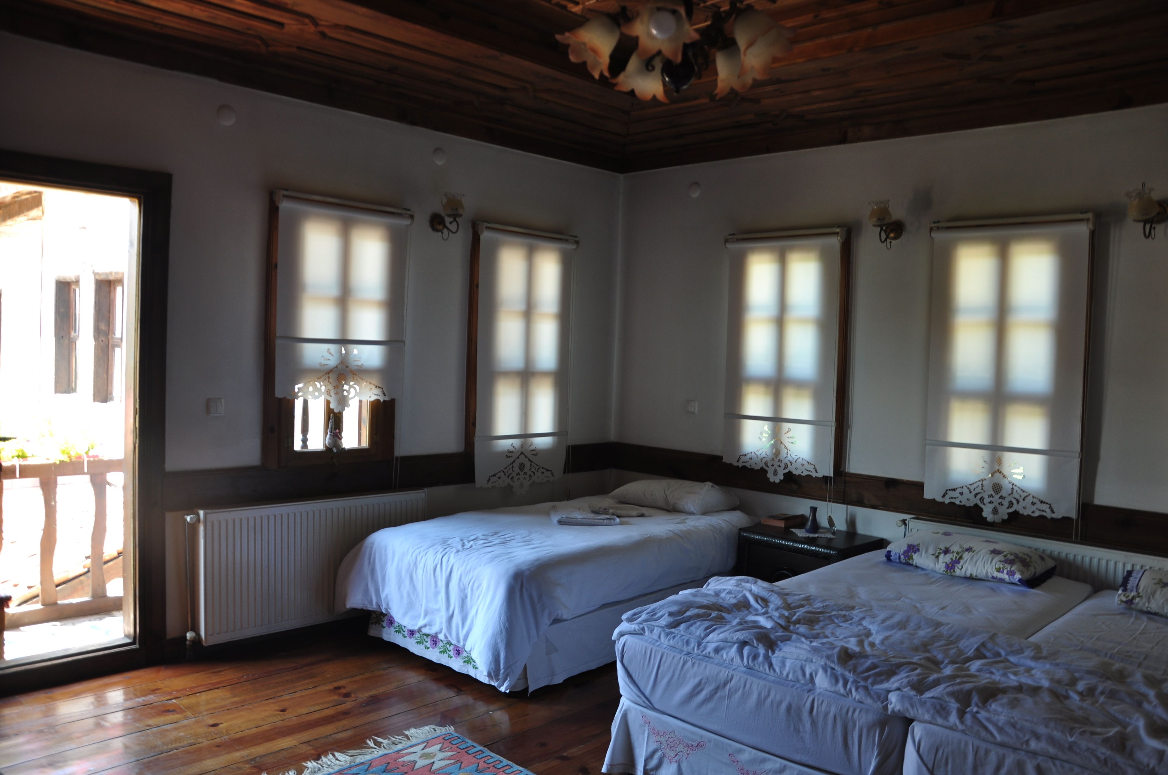 A bedroom with two beds, wooden flooring, and large windows with white curtains.