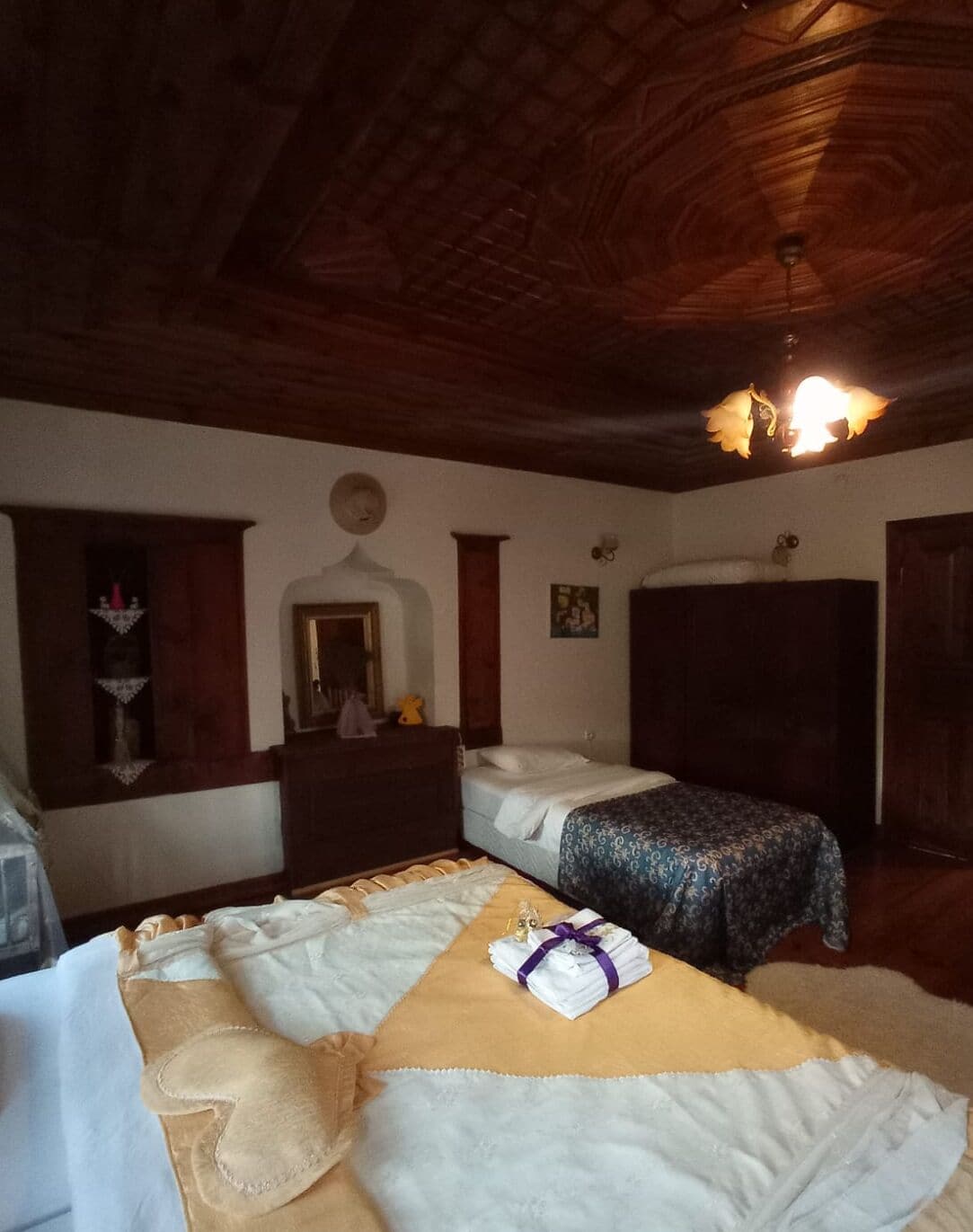 A cozy room with two beds, wooden ceiling, and a small table with a lamp.
