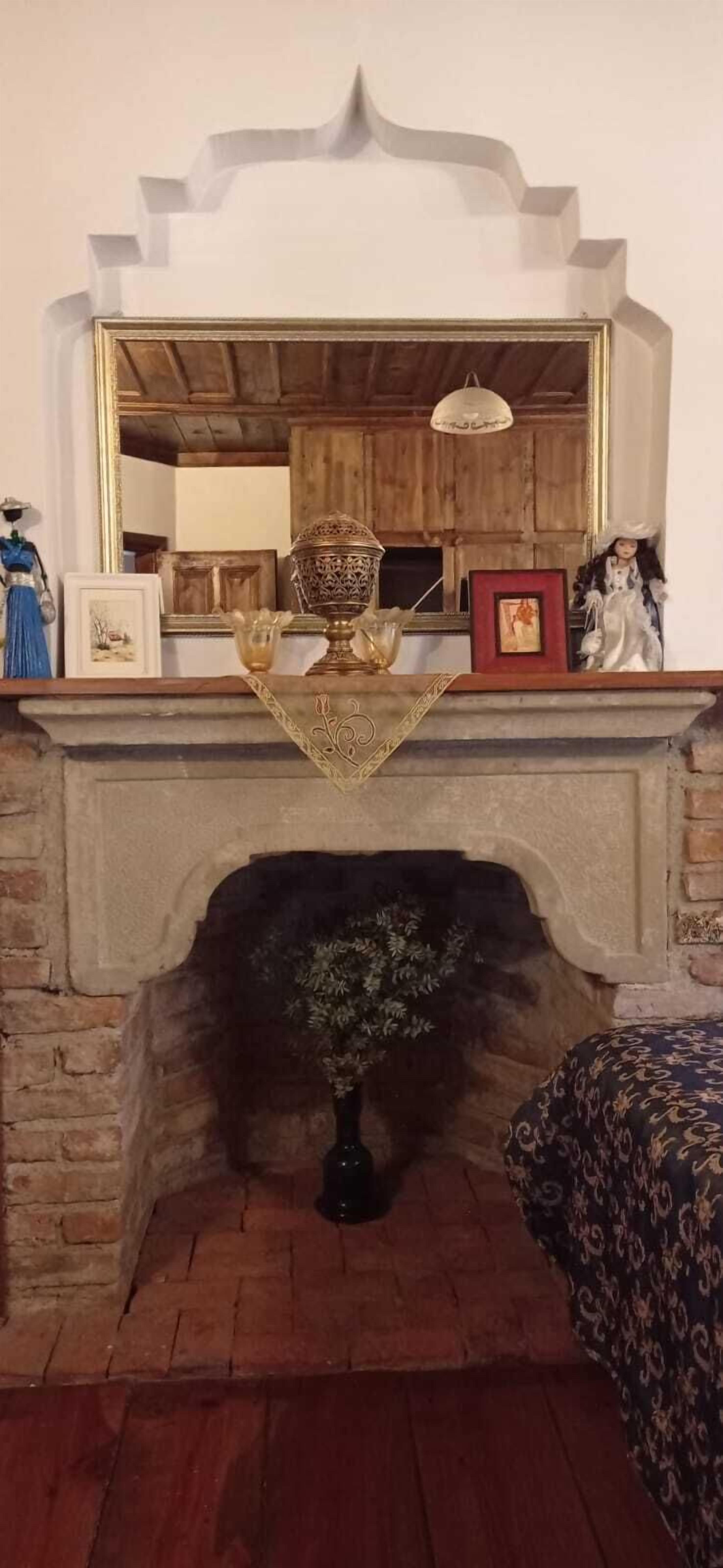 A fireplace with a vase of dried flowers, a framed picture, and a decorative bowl on the mantel.