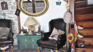A traditional room with a wooden staircase, a green chest of drawers, two leather armchairs, a mirror, and a lamp.