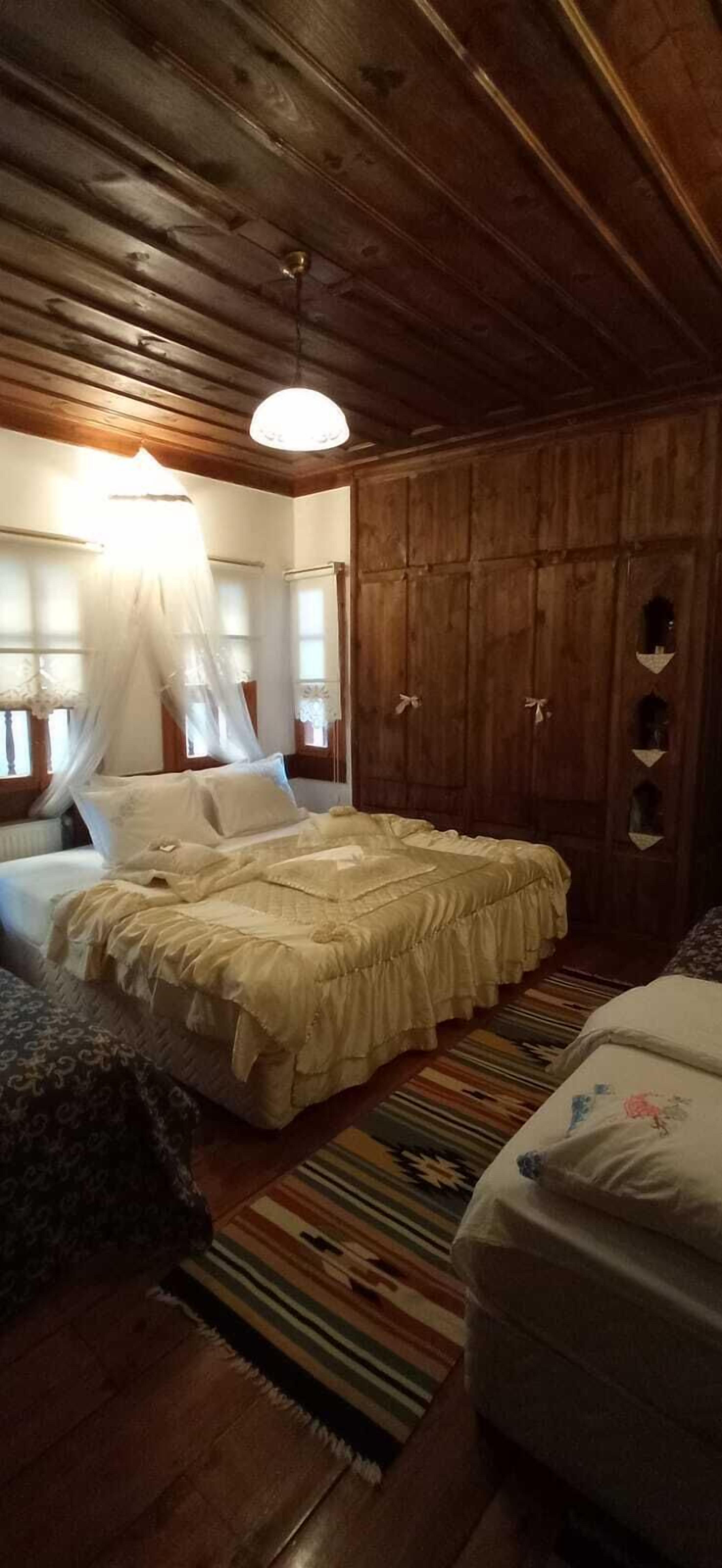 A bedroom with a wooden ceiling, a canopy bed, a wardrobe, and a striped rug.