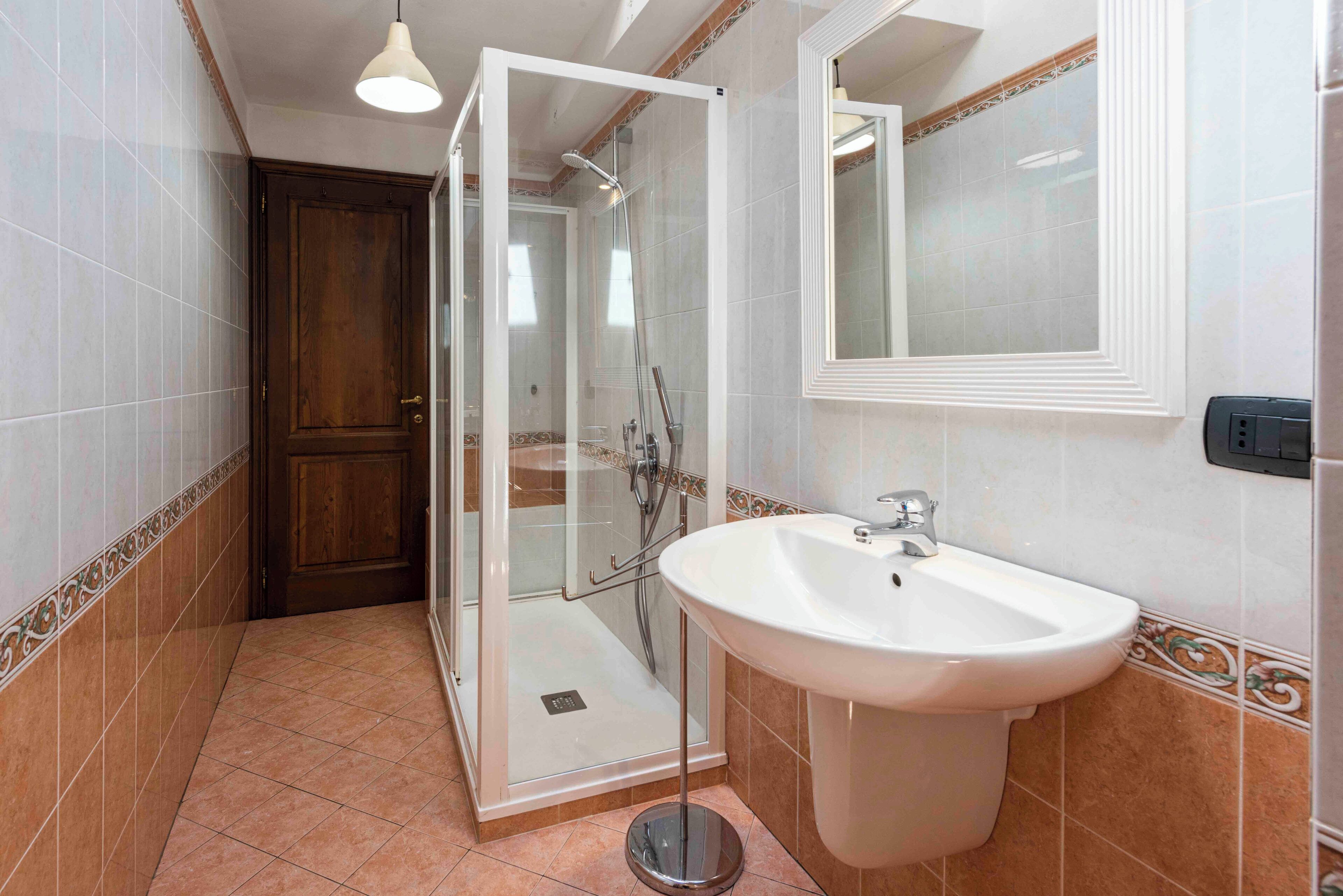 A bathroom with a glass-enclosed shower, a sink, and a mirror.