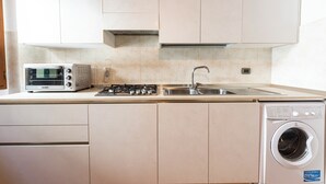 Een keuken met een inbouwtoaster, fornuis, spoelbak en wasmachine.