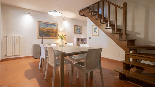 Een eethoek met een houten trap, witte stoelen, een tafel en een radiator.
