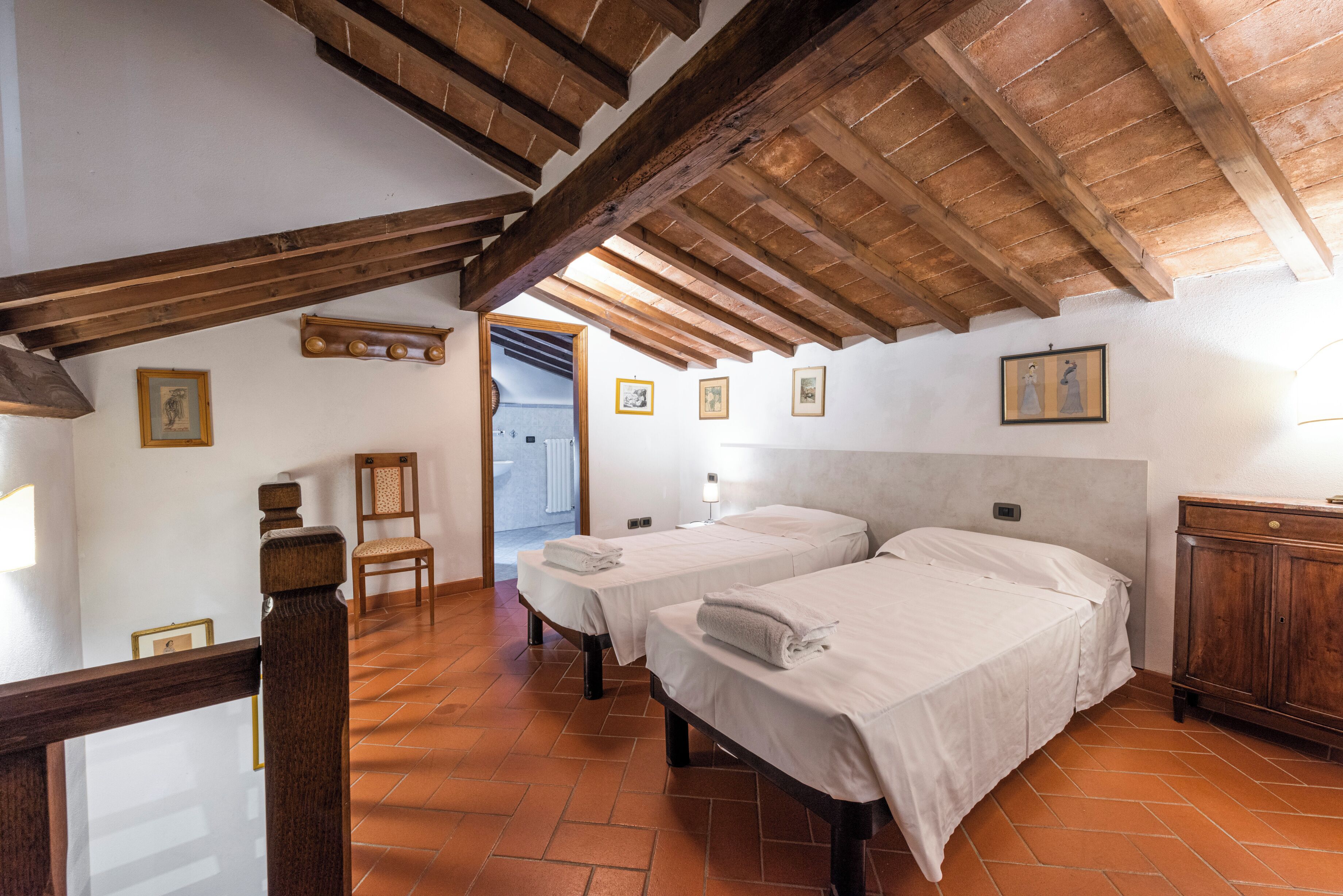 A room with two beds, wooden beams, white walls, and a tiled floor.